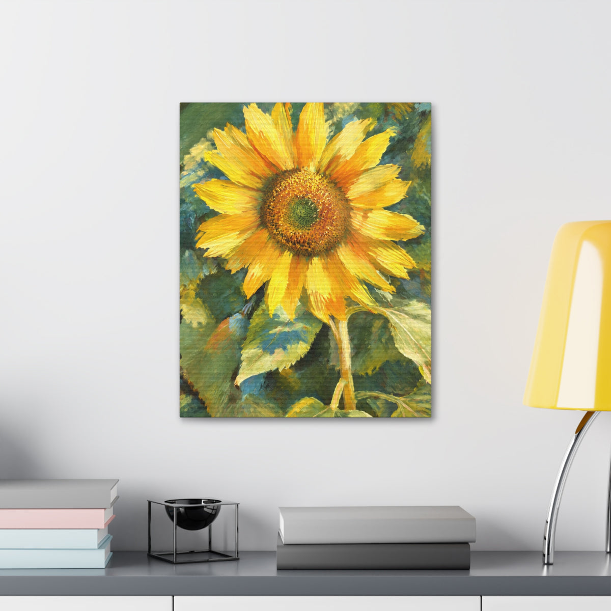 Wider Sunward sunflower canvas above a gray cabinet with stacked books and a yellow table lamp.